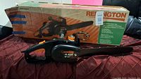 Electric chain saw on red quilted surface with original box behind