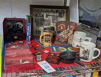 Overview of lot items including game cartridges, mugs, firefighter statue, framed firefighting memorabilia, and cast iron skillet