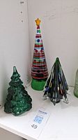 Shows three Christmas tree shaped glass candle holders in green, colorful, and multi-color variants with star topper