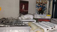 Photo showing Nintendo Wii console, white Wii remotes, nunchuck controllers, sensor bar, and Elvis Aloha From Hawaii Special VHS tape.