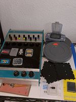 Wide shot showing Electro Lab Design Console with colorful knobs, PlayStation memory card, Gameboy games, camera remote, and plastic transparent cases containing memory cards