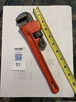 Photo of a 10-inch pipe wrench with orange handle next to yellow measuring tape showing length around 10 inches.
