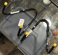 Two black metal Hang All wall hooks with yellow caps, placed on a plastic container with tiled floor beneath.