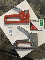 Photo showing two staple guns stacked on each other: one red and one silver, with a box of Arrow JT21 insulated staples nearby.
