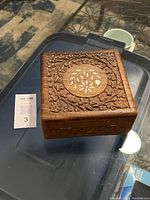 Closed view of the carved wooden jewelry box showing floral and vine patterns on the lid with central circular inlay.