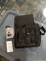 Black electrician and handyman tool pouch placed on a surface with a MaxSold tag beside it, showing pocket arrangement and clip.