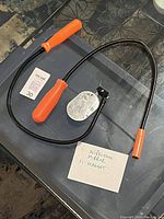 Photo showing a flexible inspection mirror with an orange handle and a magnetic pickup tool placed on a glass surface with a note describing items.
