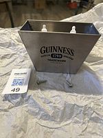 Metal Guinness bottle cap catcher with two screws for mounting placed in front on a cloth background.