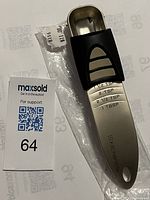 Photo showing a new adjustable stainless steel measuring spoon, featuring a black measuring slide. The spoon surface is marked with measurement levels from 1/2 tsp to 1 tbsp.