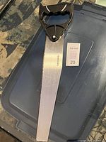 Photo of a new Husky hand saw showing the black handle and metal blade lying on a plastic bin lid outdoors.