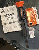 Photo showing Ramset Model HD22 powder actuated tool with orange handle and black barrel, box of 2.5 inch nails, and instruction manual on a dark surface.