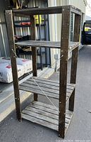 Full view of a dark stained wooden four-shelf storage unit standing outdoors near other shelving units and bags of materials.