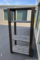 Photo of a wooden shelving unit placed outside near storage unit doors, showing its four-tier structure with solid and slatted shelves and cross-bracing.