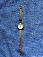 Full view of Acqua by Timex wristwatch with brown leather strap laid flat on blue textured surface