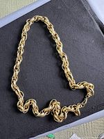 Gold plated chain necklace displayed coiled on black fabric.