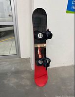 Front view of snowboard standing upright showing the red bottom and black top with bindings attached