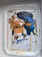 Front view of vintage metal serving tray showing Santa Claus carrying sack and Coca Cola globe with 'Wherever I go' text, white background with wear and rust