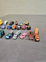 Wide view of 18 assorted vintage toy cars including trucks, race cars, buses, and specialty vehicles in various colors and designs.