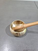 Brass singing bowl with wooden mallet resting inside, shown from a high angle on grey surface.