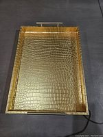 Gold tray with crocodile texture and metal handles on each side, rectangular shape.