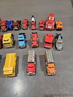 Photo showing 18 assorted vintage die-cast toy cars including trucks, race cars, and utility vehicles in colors red, blue, yellow, and orange.