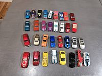Top-down view of 32 vintage toy cars arranged on grey surface showing variety of colors and types