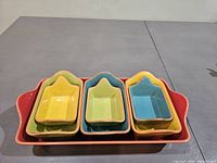 Photo showing set of one large red rectangular ceramic tray holding four smaller nesting baking dishes in yellow, green, and blue colors.
