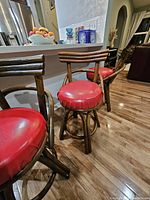 Three vintage bamboo swivel bar stools with red vinyl cushions positioned near a kitchen island on a hardwood floor under indoor lighting.