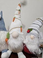 Four seasonal gnomes with distinct hats: blue sunflower themed, white carrot embroidered, red and white winter pattern, and grey and white with holly.