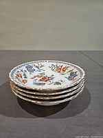 Stack of four dessert plates showing colorful floral pattern and gold trim on scalloped edges