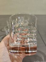 Close-up of one whiskey tumbler held in hand showing clear crystal glass with horizontal etched stripes and thick solid base.