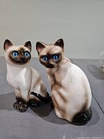 Pair of vintage Goebel Siamese cat porcelain figurines, showing blue eyes and realistic color gradient.