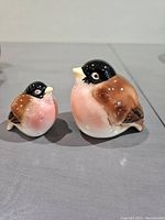 Two vintage Japanese bird-shaped salt and pepper shakers with brown and pink painted ceramic body, black heads and yellow beaks, placed on a flat surface.