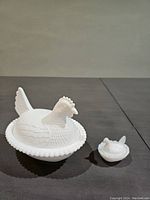 Front view of two milk glass hen-on-nest covered dishes, one larger with beaded edge, one smaller without beaded edge.