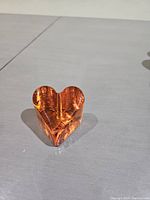 Top angle photo showing the vibrant orange glass heart-shaped paperweight on a flat surface.