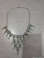 Full view of the vintage-inspired necklace with silver-tone metalwork and green oval cabochon stones shown flat on fabric background.
