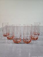 Six vintage highball glasses arranged in a row, showing front and side views. Glasses have a clear body with pink tint at the base, cylindrical shape, and smooth surface.