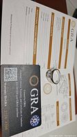 Moissanite ring placed on GRA grading certificate and warranty card, showing authenticity and grading details.