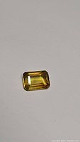 Photo of single emerald cut golden yellow sapphire on plain background showing cut, facets, and color