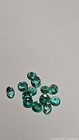 Close-up photo of multiple round cut natural Columbian emerald gemstones, showing their vivid green color and faceted brilliance.