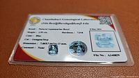 Photo showing the certified natural aquamarine beryl gemstone along with its certification card from Chanthaburi Gemological Laboratory.