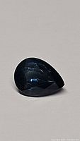 Close-up photo of the pear-shaped blue sapphire gemstone showing facets and deep blue color.
