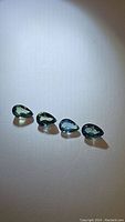 Four pear cut multicolored sapphires shown lying flat under light displaying teal blue coloration, clarity, and faceting.