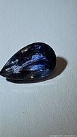 Close-up photo of a pear-shaped blue sapphire gemstone, showing its deep cornflower denim blue color with good transparency and clarity.