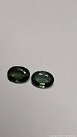 Pair of oval cut green sapphires displayed on white background, showing color and cut.