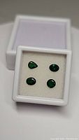 Four loose tsavorite garnet gemstones displayed in a white gem box, showing vivid green color and cut shapes.