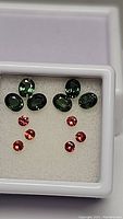 Photo showing five oval cut green sapphires and five round orange sapphires arranged in a display box on a white padded background.