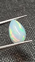 Close-up image of pear-shaped cabochon Ethiopian opal with visible multicolored play-of-color, held by tweezers on black textured background