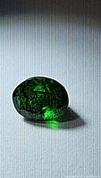 Oval cut green tsavorite garnet gemstone photographed on a lined white surface showing inclusions and color depth.