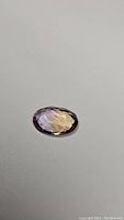 Oval cut ametrine gemstone shown on plain background to highlight color and clarity.